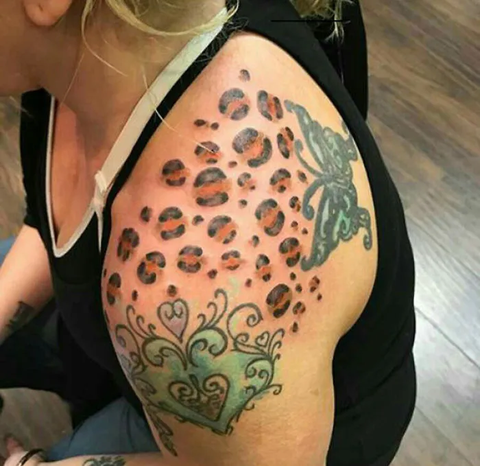Woman's shoulder with a leopard print tattoo and green design, exemplifying bad tattoo fails.