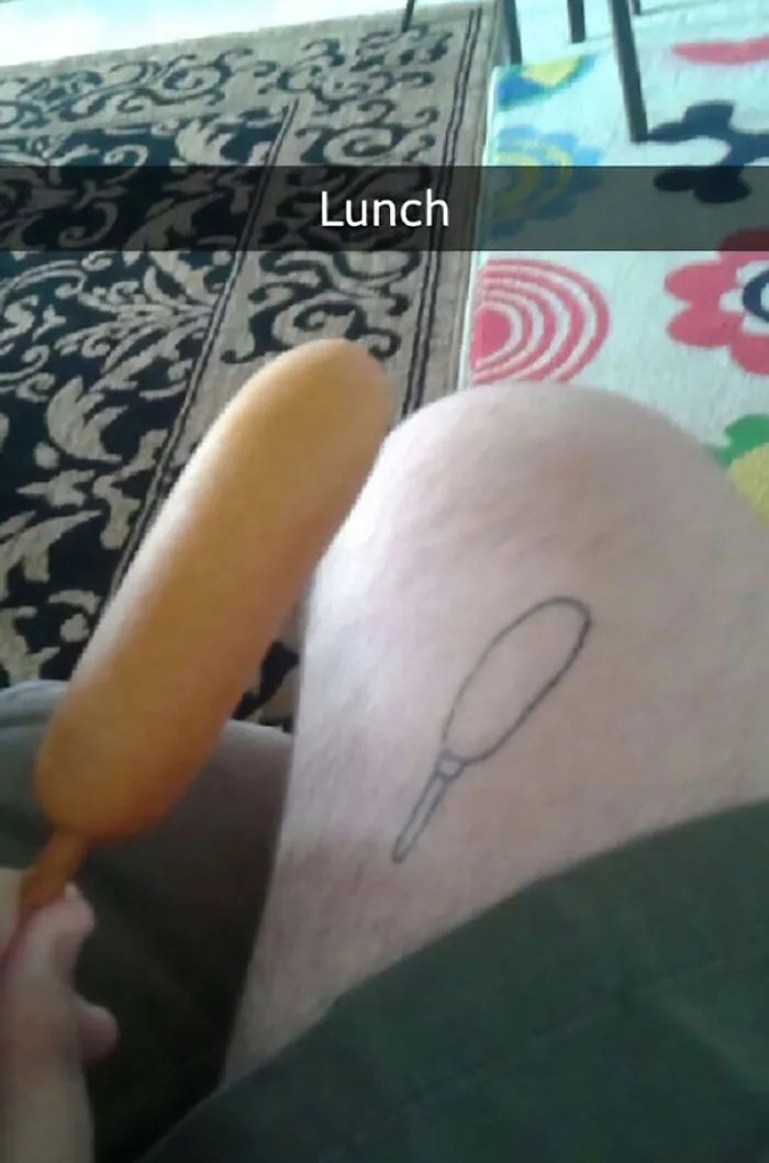 Bad tattoo fail depicting a simple corn dog design on a leg, with an actual corn dog held nearby.