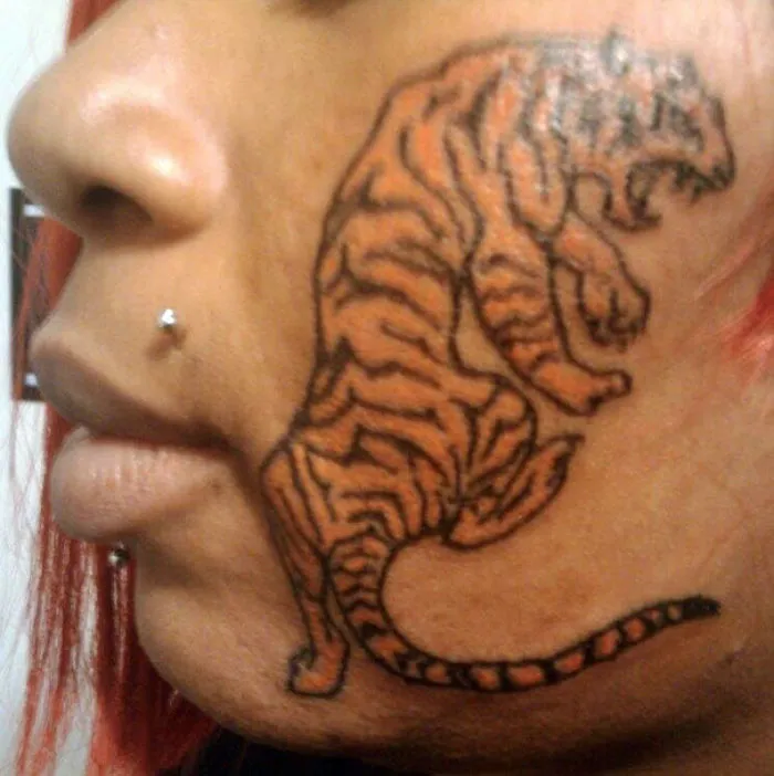 Face tattoo fail with a tiger design covering the cheek, highlighting a humorous and cringe-worthy tattoo choice.