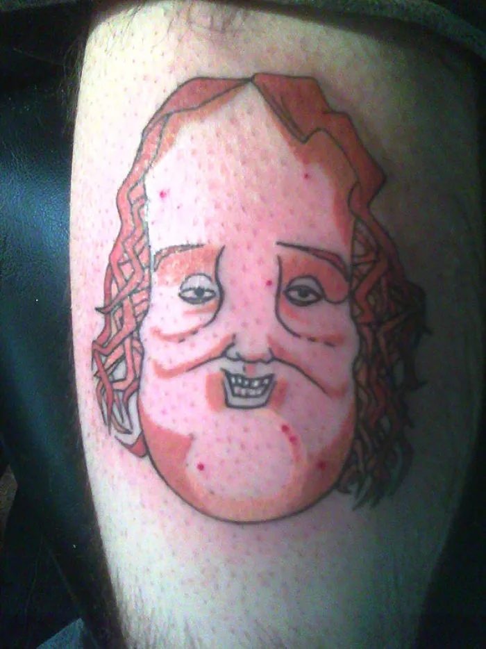 Bad tattoo fail showing a distorted face with curly hair, creating an unusual and humorous appearance.