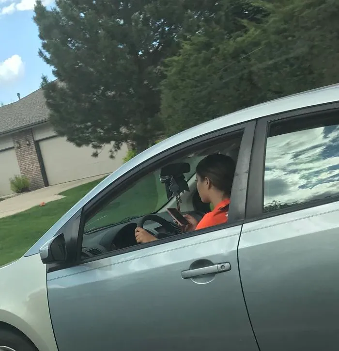She Was Snapchating While Driving (40 Mph Road(64.4 Kph)). She Also Had A Little Brother In The Passenger Seat While Doing This. Hate How Often I See People Doing Stuff Like This (Photo Taken By A Passenger Of My Car)