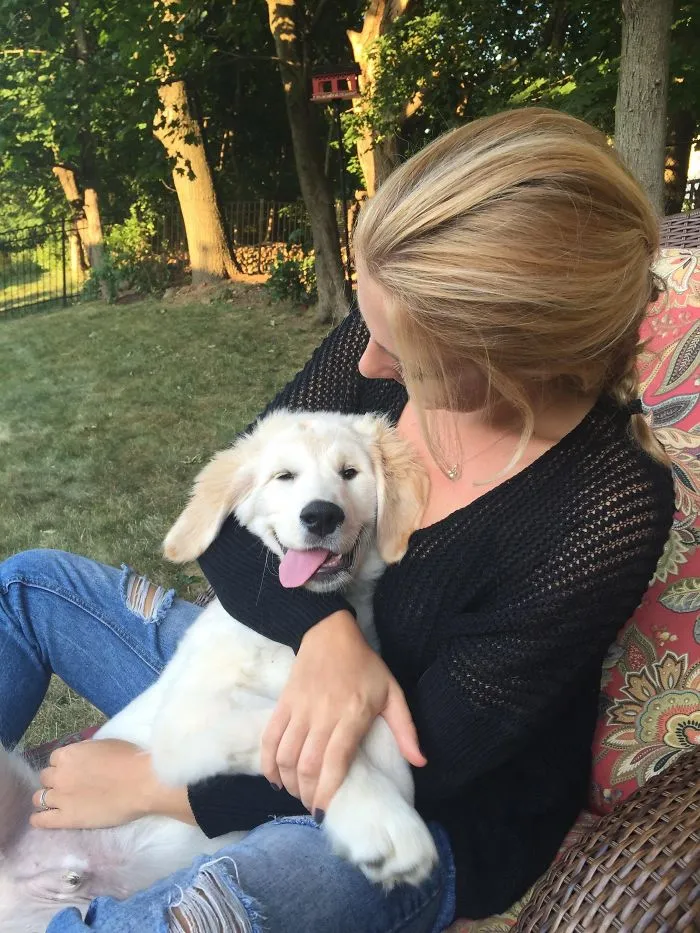 A woman cuddling a cute puppy outdoors, both looking happy and relaxed in a garden setting.