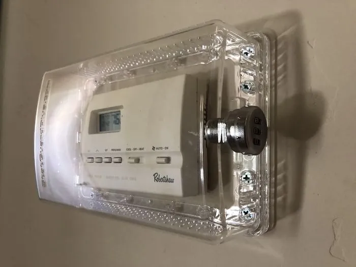 Thermostat locked in a clear case with a combination lock, showcasing a dad's humorous solution.