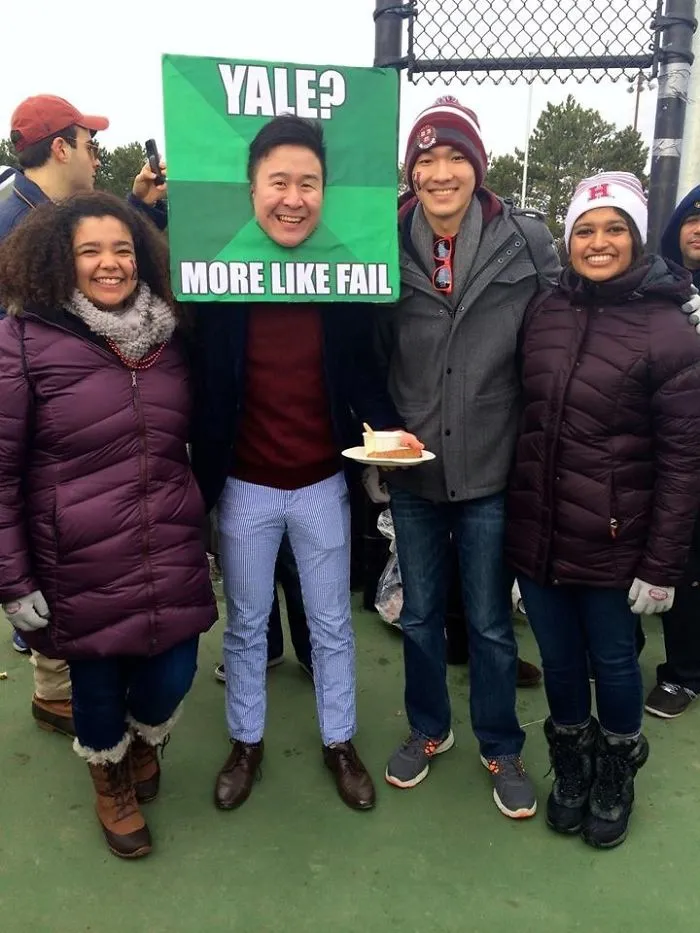 Man at an event with a humorous "Yale? More Like Fail" sign, standing with friends, showcasing funny dads' humor.