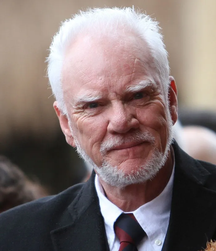 Malcolm McDowell wearing suit and smiling