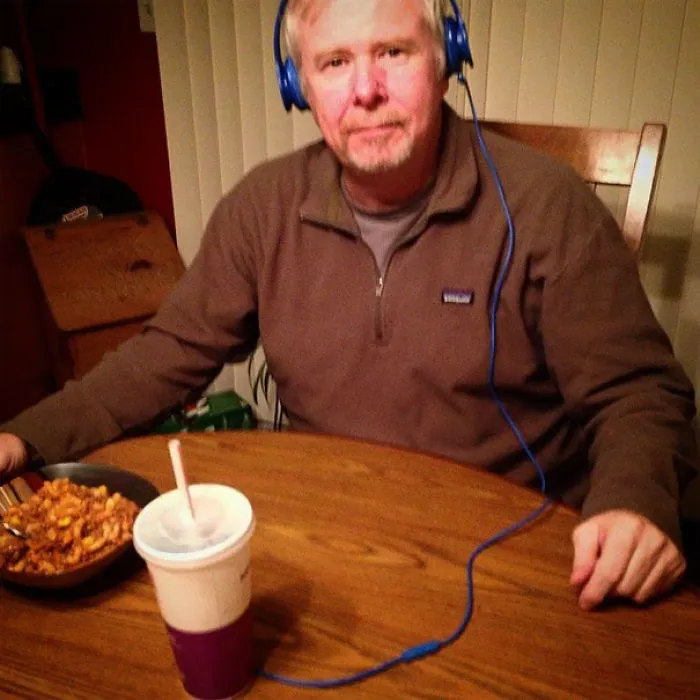 A dad humorously using pasta as headphones while seated at a table.