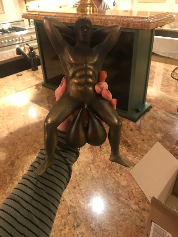 A person holding a humorous bronze sculpture in a kitchen.