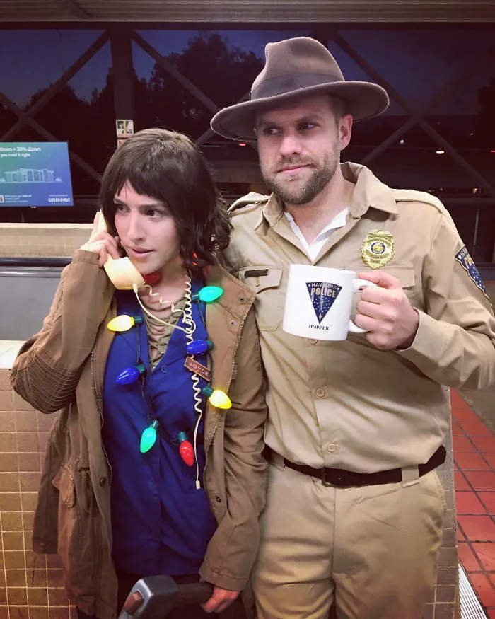 Couple in creative Halloween costumes, one with Christmas lights and phone, the other in a sheriff uniform with a mug.