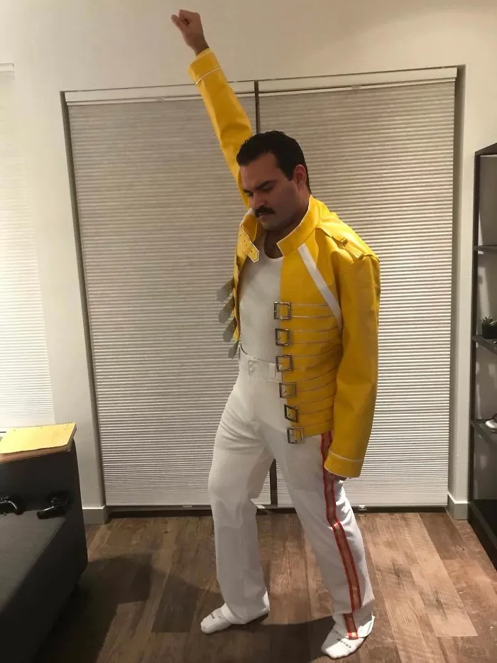 Man wearing a yellow jacket recreating Freddie Mercury's iconic pose as a Halloween costume