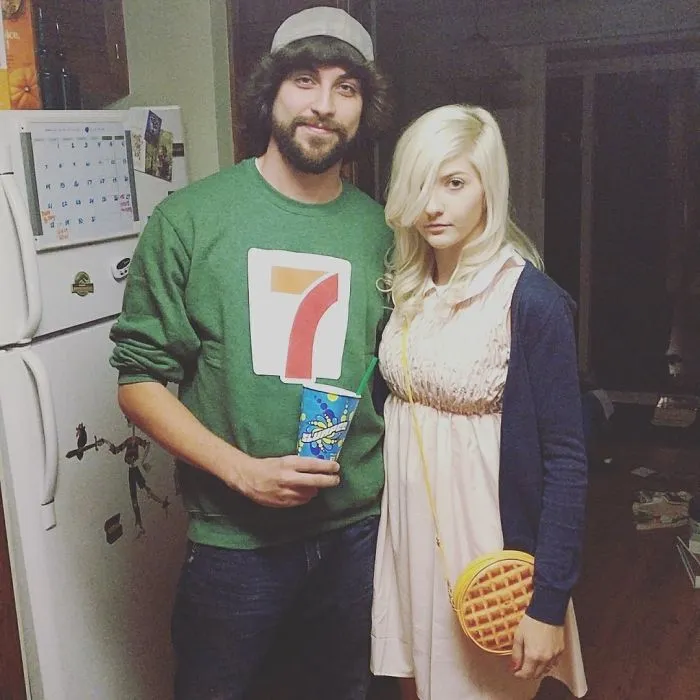 Couple in Halloween costumes, with a man in a 7-Eleven shirt and a woman with a waffle purse, winning Halloween style.