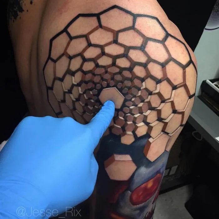 3D tattoo of hexagons creating an optical illusion, with a gloved hand touching it on a shoulder.
