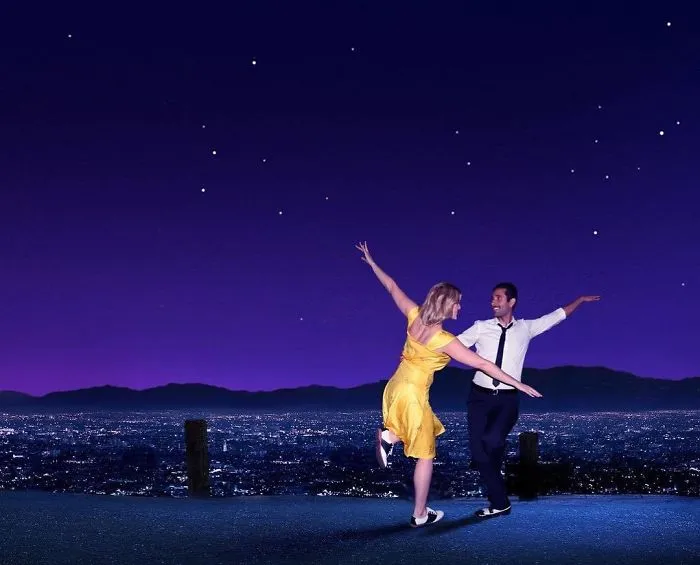 A couple dressed as La La Land characters dancing under a starry sky for a creative couples Halloween costume idea.