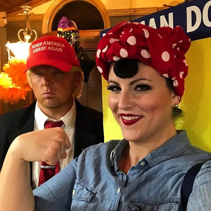 Couple in creative Halloween costumes, one in a red MAGA hat and suit, the other in a vintage polka dot headscarf.