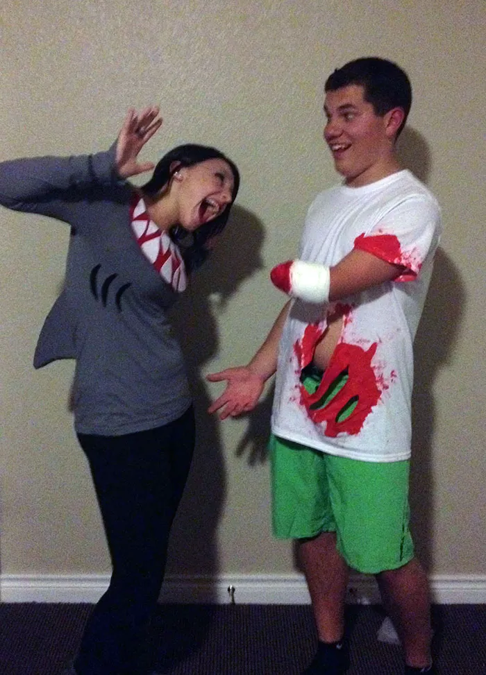 Couple in creative Halloween attire, with one person in a shark costume and the other appearing to have a bitten arm.