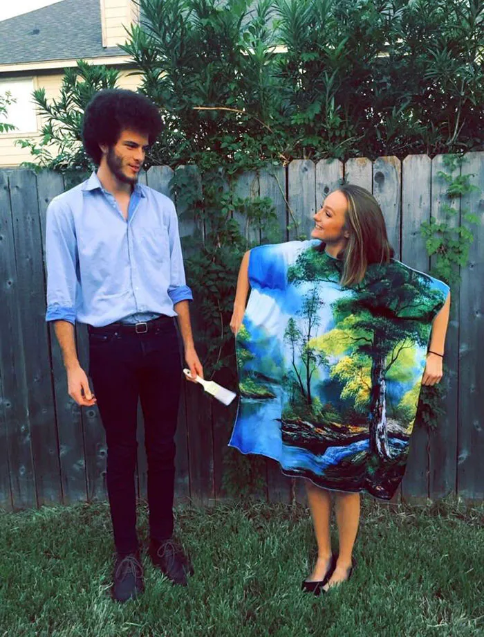 Couple dressed as Bob Ross and painting, perfect Halloween costume idea, standing in a backyard with a wooden fence.