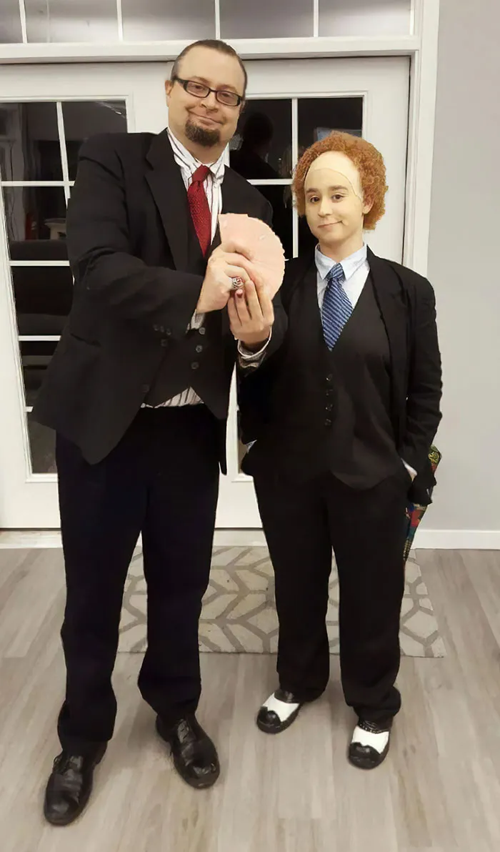 Couple dressed in matching costumes, holding a prop, celebrating Halloween.