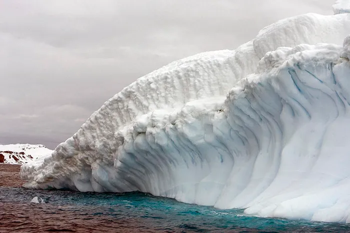 Massive ice formation with detailed textures floating in dark waters, showcasing amazing Antarctica natural landscape facts.