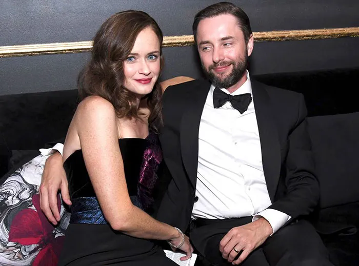 Couple dressed formally sitting closely on a couch, representing celebrities who fell in love while acting together.