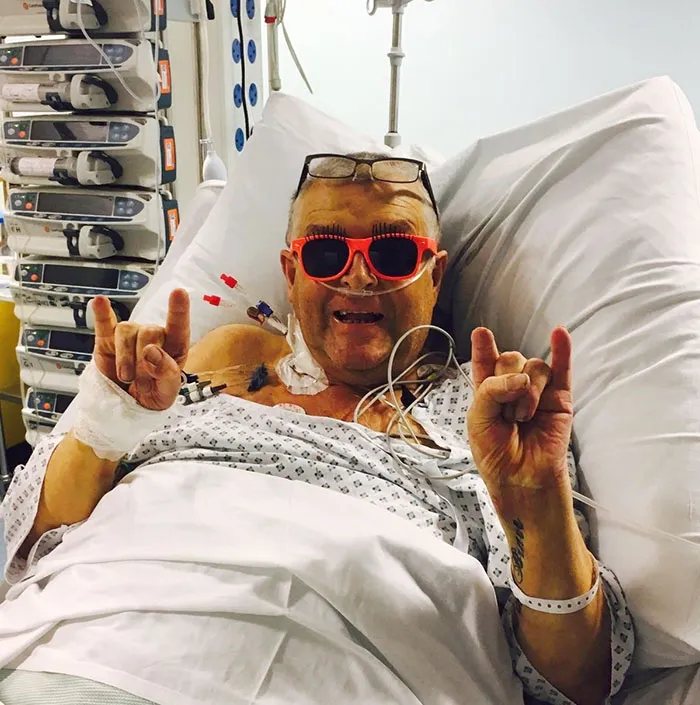 Man laying in a hospital bed and doing funny poses for a picture 