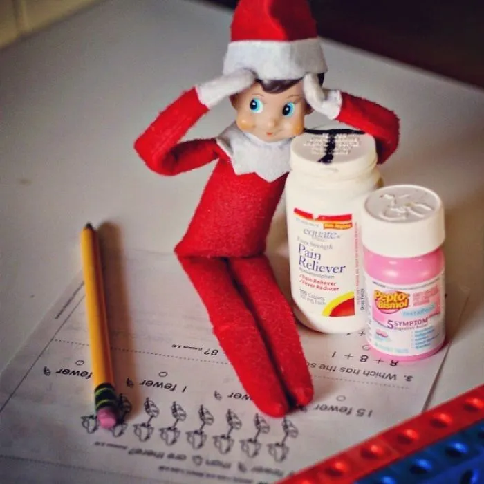 Elf On The Shelf idea with elf holding head in stress beside pain reliever, stomach medicine, worksheet, and pencil.
