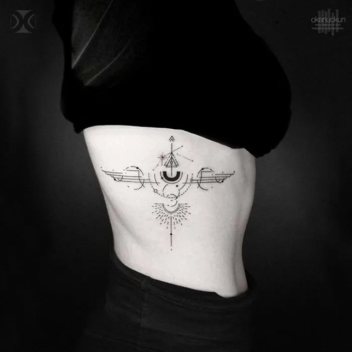 Geometric tattoo on a person's side by Turkish artist Okan Uçkun, featuring intricate symmetrical designs.