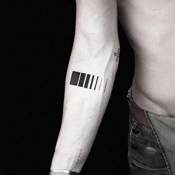 Geometric tattoo by Turkish artist Okan Uçkun on a person's forearm, featuring a series of rectangles and lines.