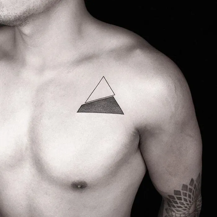 Geometric tattoo by Turkish artist Okan Uçkun on a person's chest, featuring a triangle design.