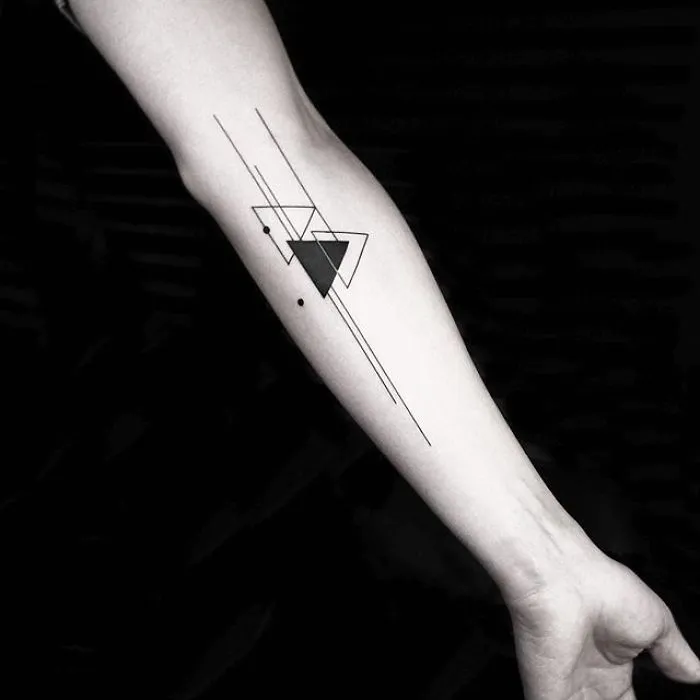 Geometric tattoo by Turkish artist Okan Uçkun on a forearm, featuring intersecting triangles and lines.