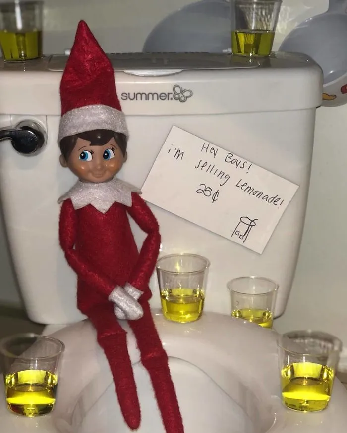 Elf on the Shelf sitting on toilet selling lemonade in cups with a sign for 25 cents as a mischievous holiday idea.