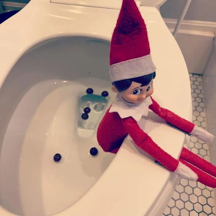 Elf On The Shelf prank idea with elf sitting on toilet edge surrounded by chocolate candy pieces for mischief.