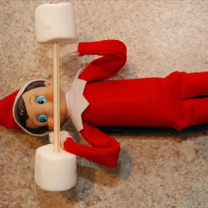 Elf On The Shelf lifting a marshmallow barbell in a creative and playful weightlifting mischief idea.