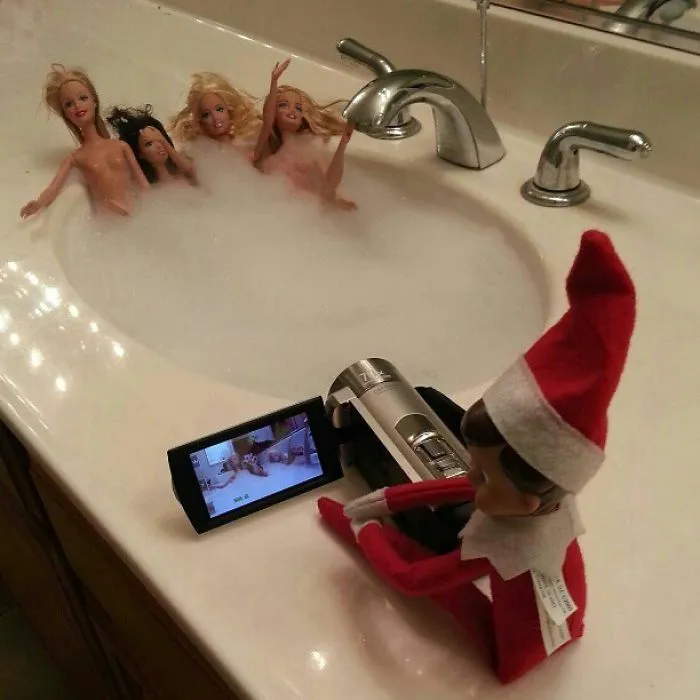 Elf On The Shelf filming fashion dolls in a bubble bath inside a sink for a playful holiday mischief scene.