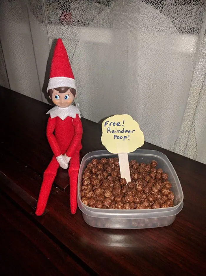 Elf on the Shelf next to a container of cocoa cereal labeled free reindeer poop for a playful holiday mischief idea.