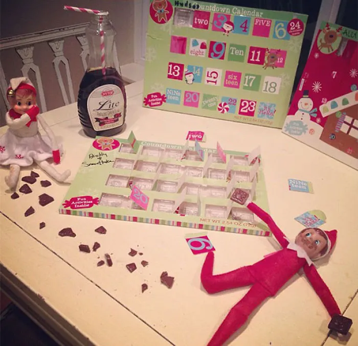 Two Elf On The Shelf dolls raiding an advent calendar with chocolate scattered and one holding a syrup bottle for mischief ideas.
