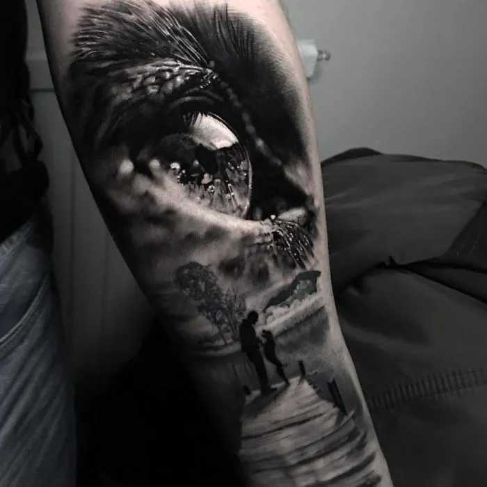 Realistic eye tattoo with landscape and figures on forearm, showcasing creative ink ideas.