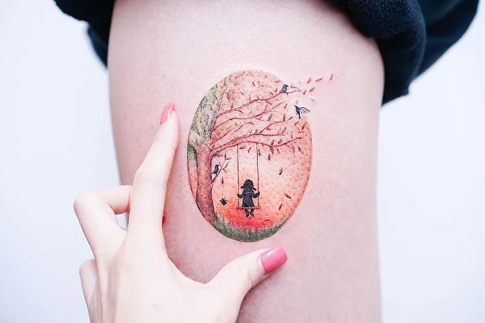 Hand pointing to a tattoo with a tree and swing design, ideal for every ink lover.