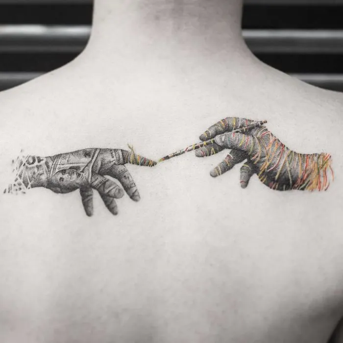 Unique tattoo design of two hands reaching toward each other on a person's back.