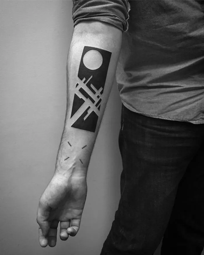 Abstract geometric tattoo on a person's forearm, featuring bold black shapes and lines.
