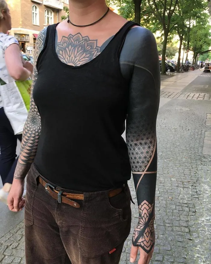 Person with intricate black geometric tattoos covering arms and chest, showcasing unique tattoo ideas on a city street.