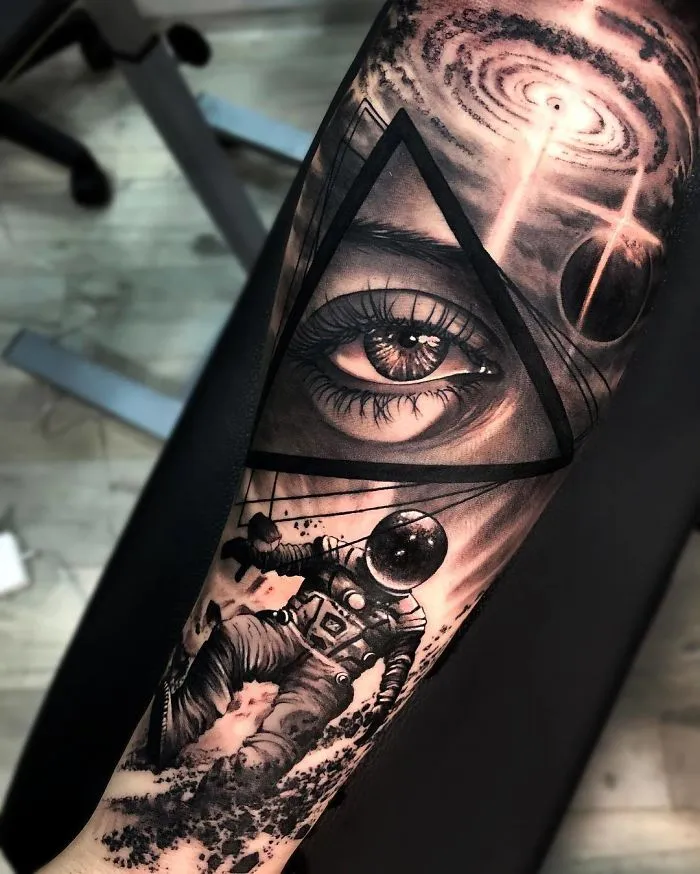 Astronaut and eye tattoo design on forearm, featuring surreal space elements for ink lovers.