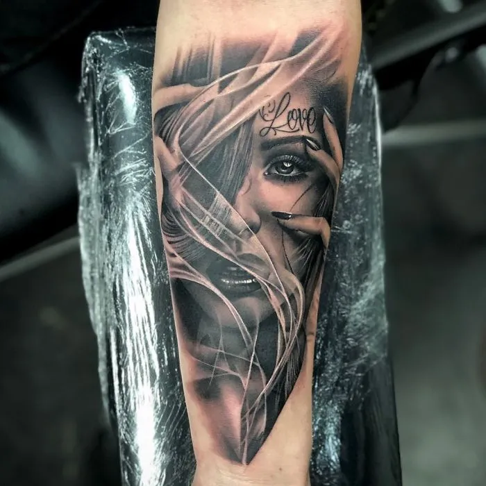 "Realistic portrait tattoo on forearm with 'Love' inscription above eye, showcasing detailed art for ink lovers."