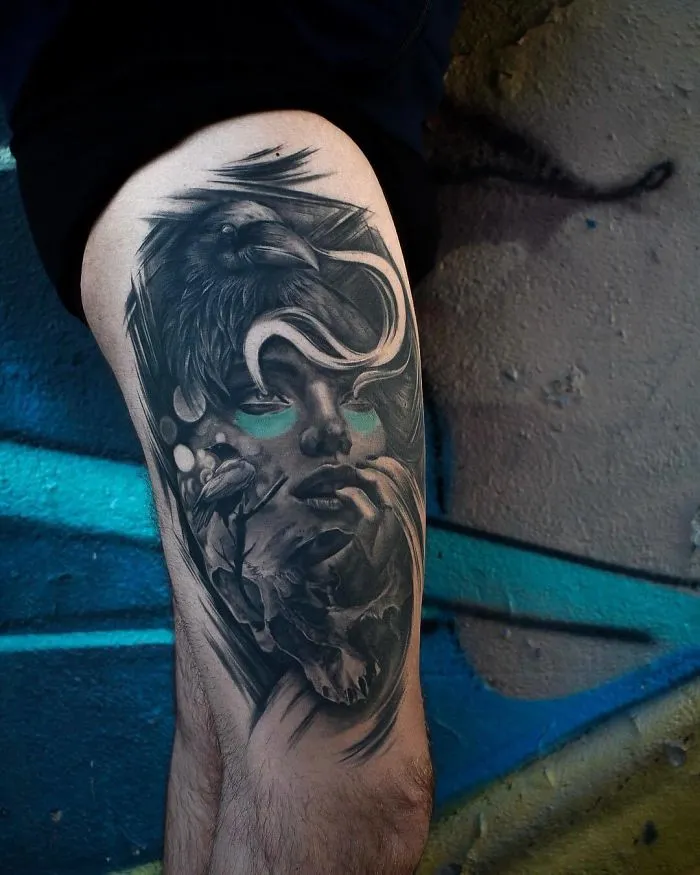 Tattoo depicting a detailed raven and abstract face design on a person's thigh, perfect for ink lovers.