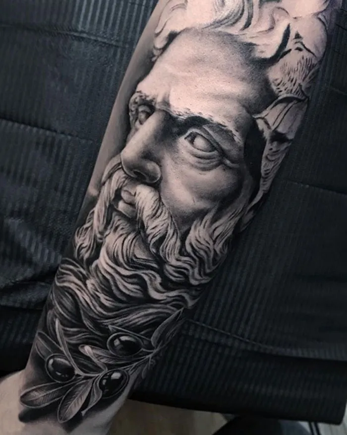 Ancient Greek statue tattoo design on forearm, featuring a detailed bearded face for ink lovers.