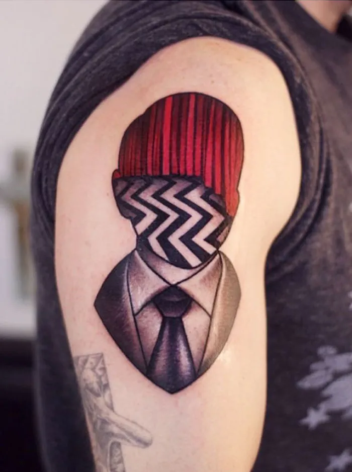 Tattoo design on arm featuring red vertical lines and black-and-white zigzag pattern on a headless suit figure.