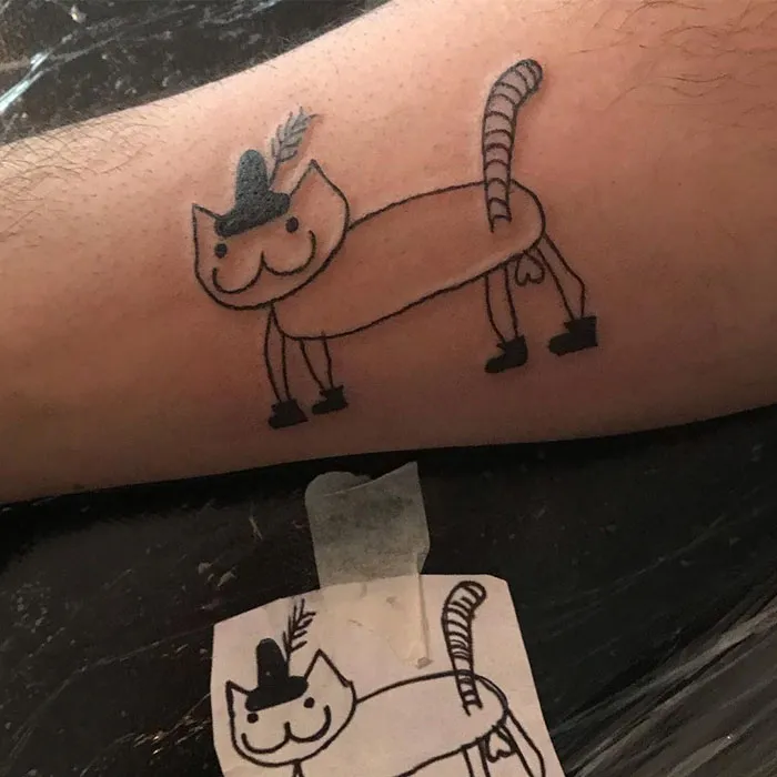 Simple cat tattoo with a hat and feather on someone's arm, showcasing unique tattoo artistry style.