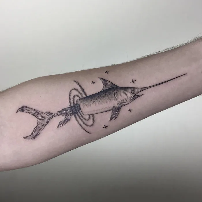 Geometric tattoo design of a swordfish on a forearm, featuring circles and stars.