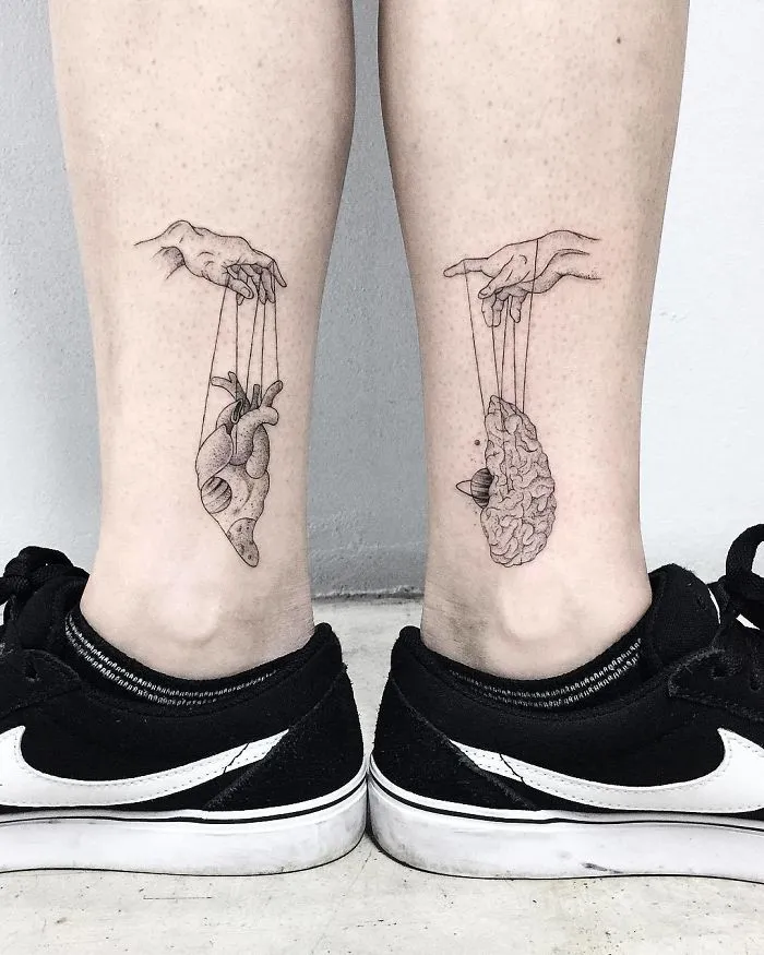 Detailed leg sleeve tattoos featuring hands controlling a heart and brain, worn by a person in black sneakers.