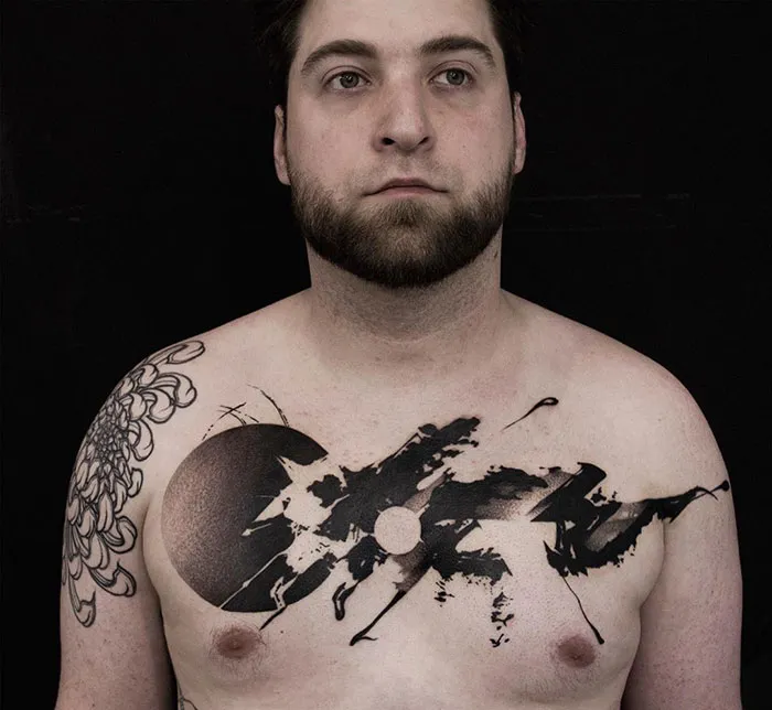 Man with an abstract black ink chest tattoo on a dark background, showcasing incredible chest tattoo ideas.