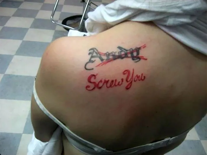 Tattoo of an ex's name covered with the words "Screw You" on a person's shoulder in a tattoo parlor.
