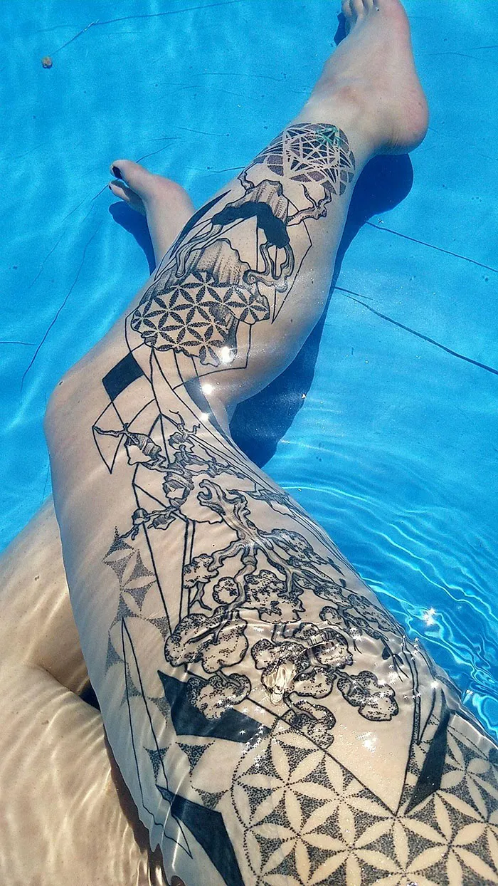 Leg sleeve tattoo with intricate black geometric and floral designs displayed underwater.